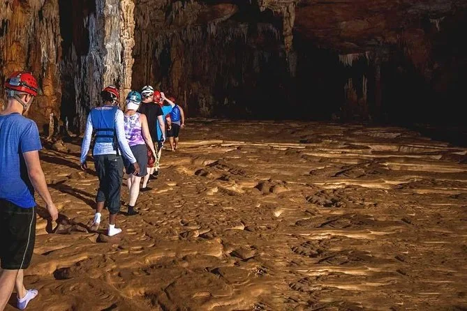 Una fila di visitatori con il casco che cammina sul pavimento a disegni di una camera asciutta della grotta