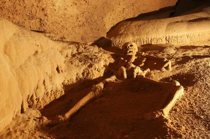 Uno scheletro ricoperto di calcite sul pavimento di una camera illuminata da una luce dorata