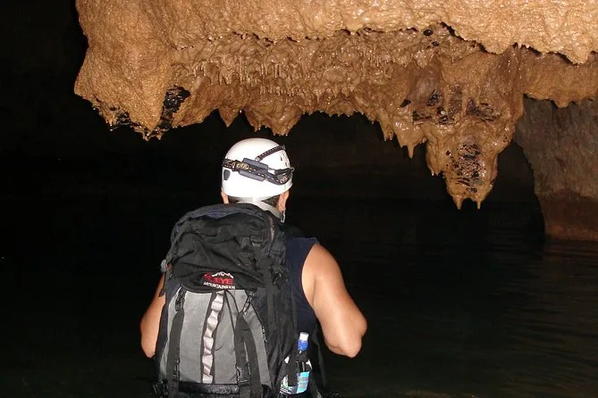 Ein Höhlenforscher mit weißem Helm und Stirnlampe, von hinten gesehen, vor Stalaktiten in einer dunklen Höhle