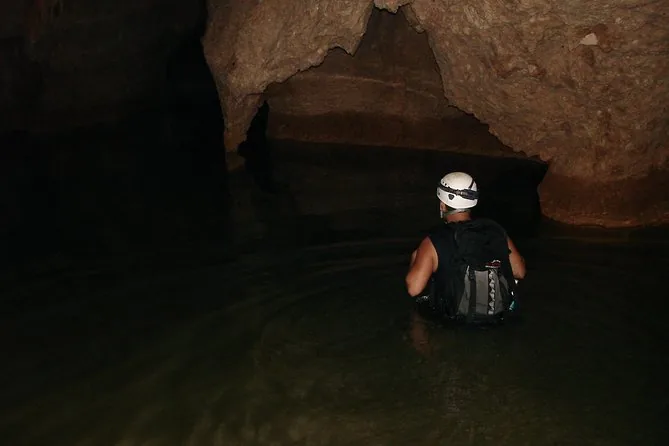 Ein Höhlenforscher mit weißem Helm watet brusttief durch dunkles Höhlenwasser