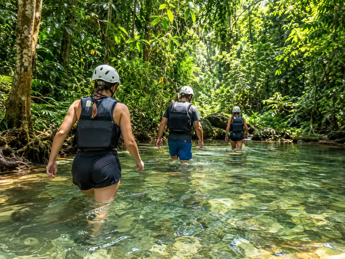 Wanderer mit Helmen und Schwimmwesten durchqueren einen klaren Dschungelbach
